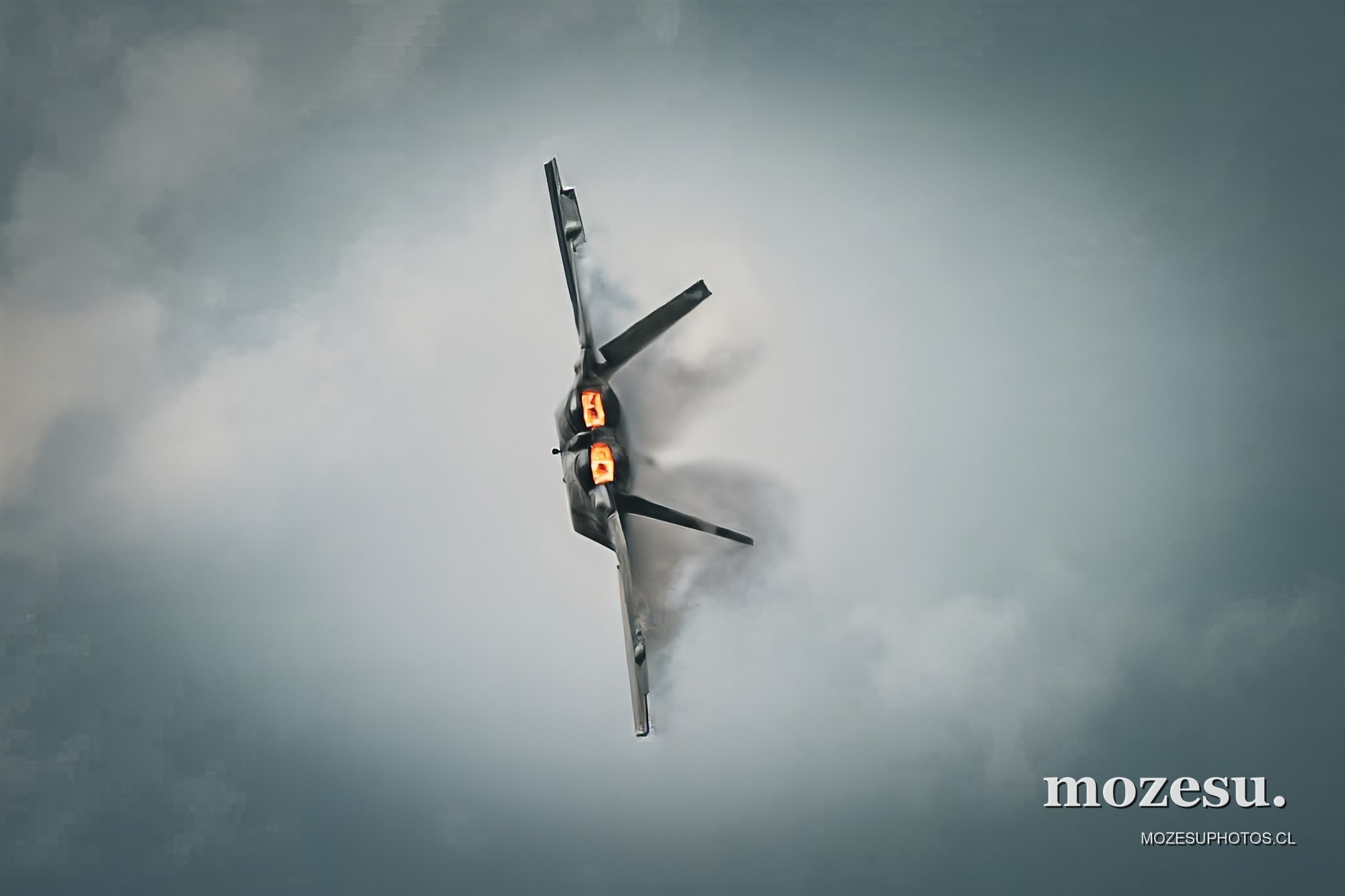 Avión de combate en un giro vertical bajo un cielo nublado.